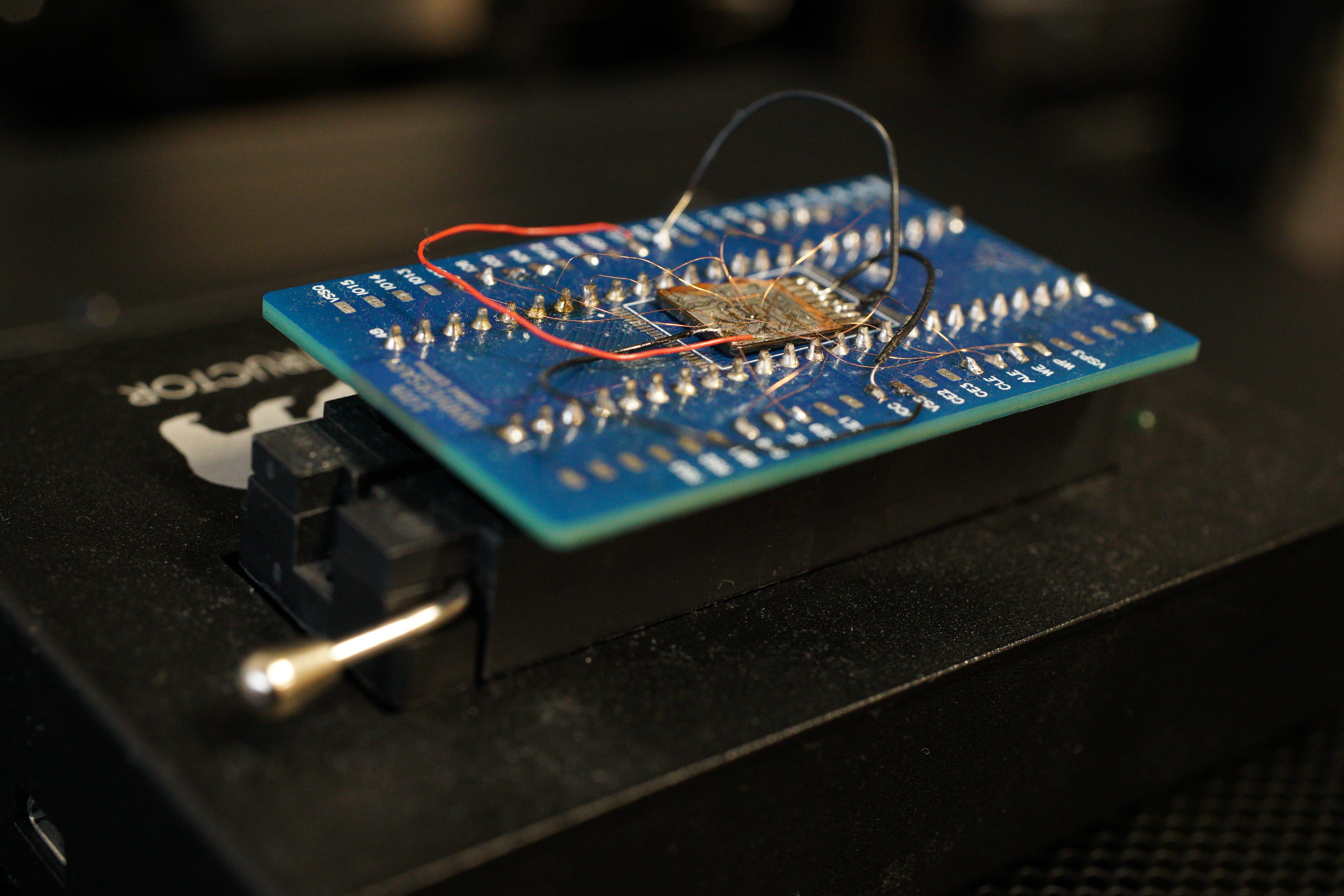 Niebieska płytka drukowana z zamontowanym układem scalonym i cienkimi przewodami, umieszczona w czarnym uchwycie serwisowym.