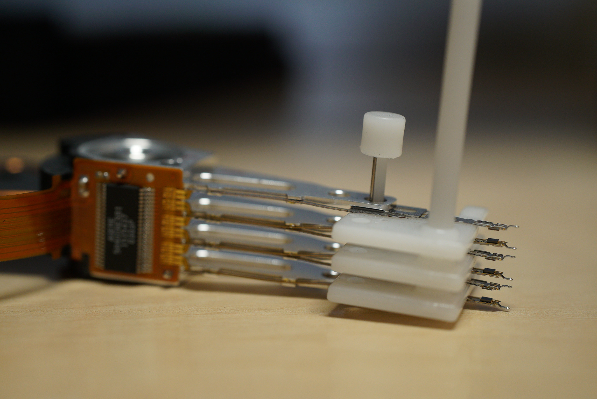 Wnętrze dysku twardego z widocznymi głowicami odczytująco-zapisującymi i elementami mocującymi, ułożone na drewnianej powierzchni.