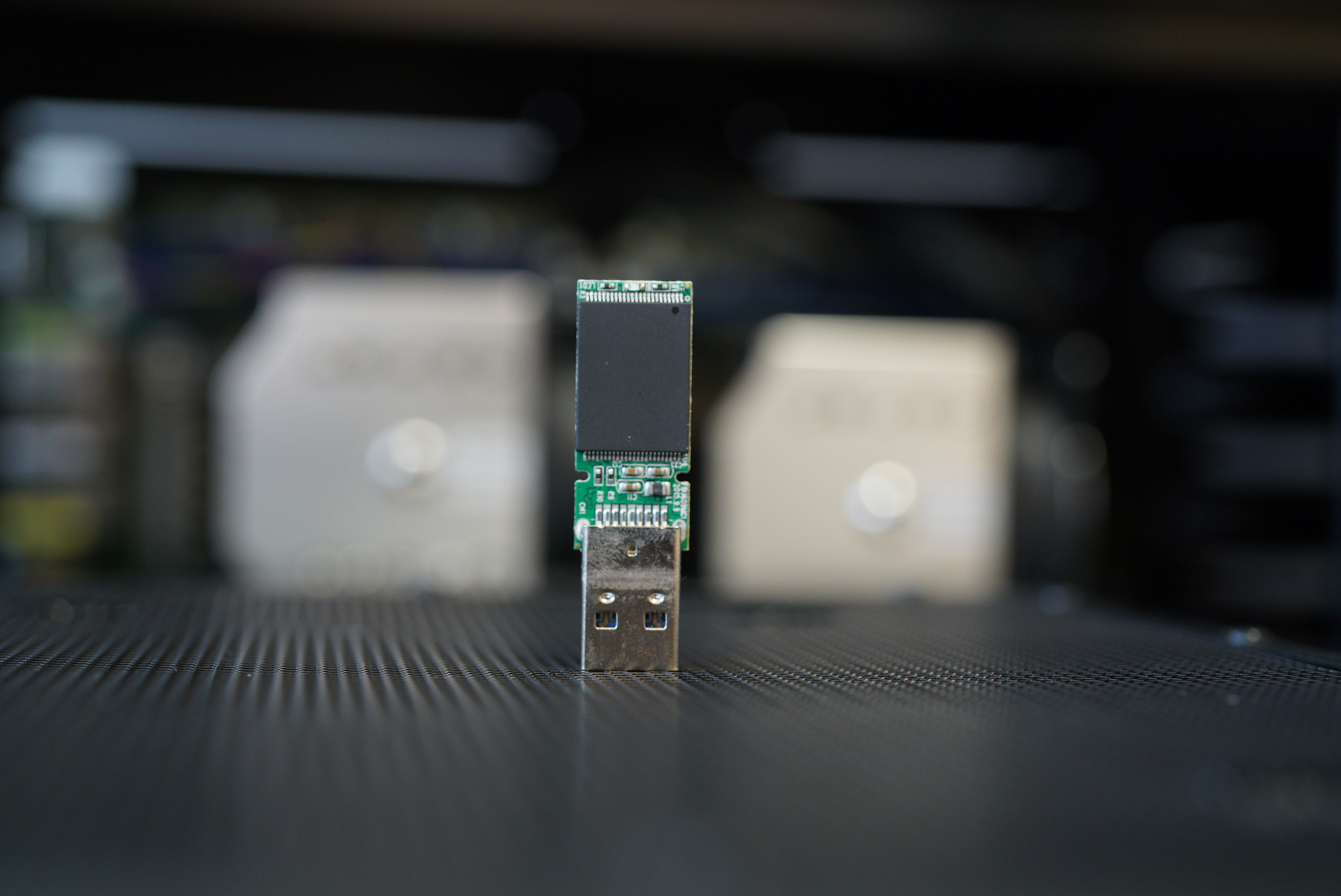 Nietypowe ujęcie modułu pamięci USB na tle rozmytych elementów wnętrza komputera, prezentujące z bliska jego konstrukcję i złącze.