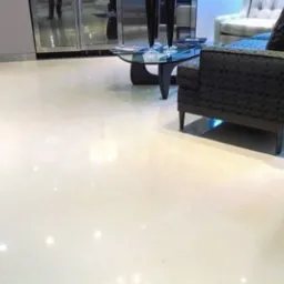 Błyszcząca, kremowa posadzka w salonie z meblami w tle, odbijająca światło, podkreślona delikatnym oświetleniem pod sofą.