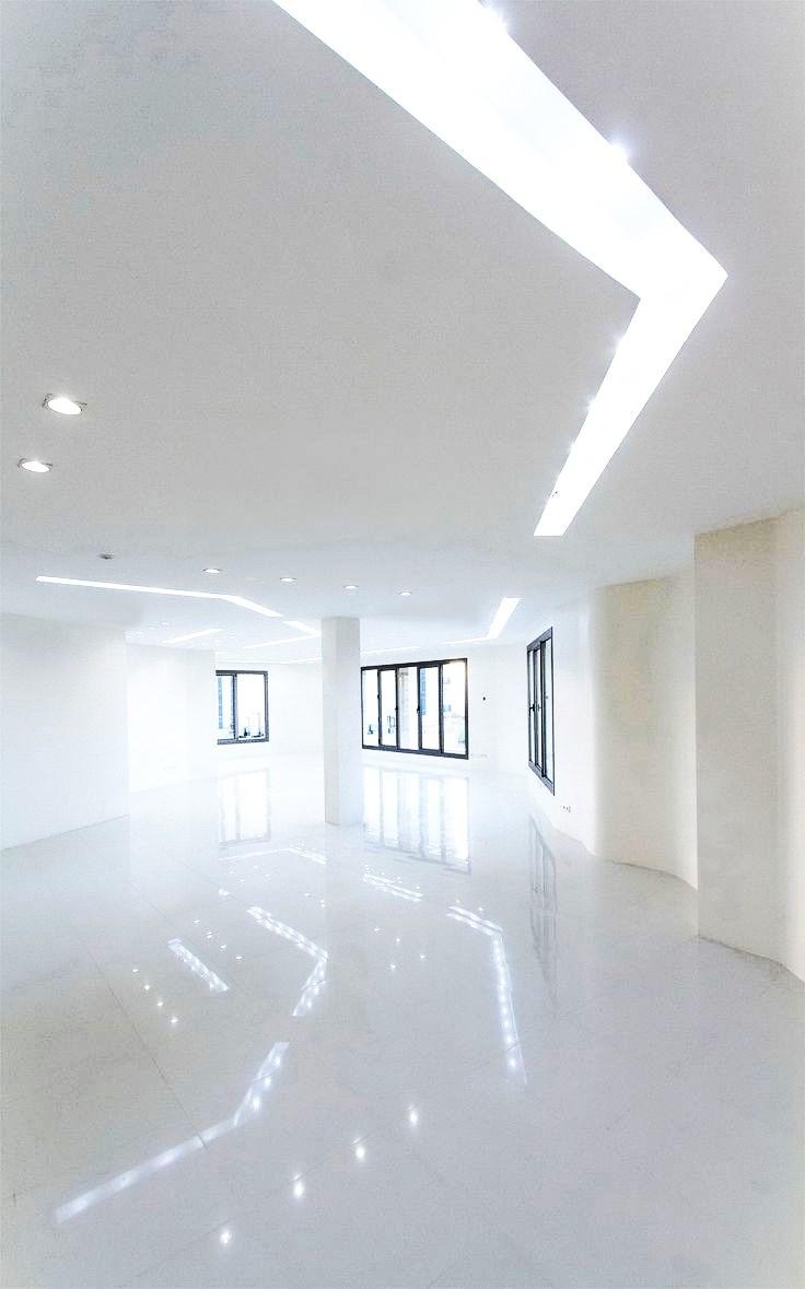 Białe, błyszczące wykończenie posadzki przemysłowej w przestronnym, jasnym pomieszczeniu z oknami i nowoczesnym oświetleniem sufitowym.