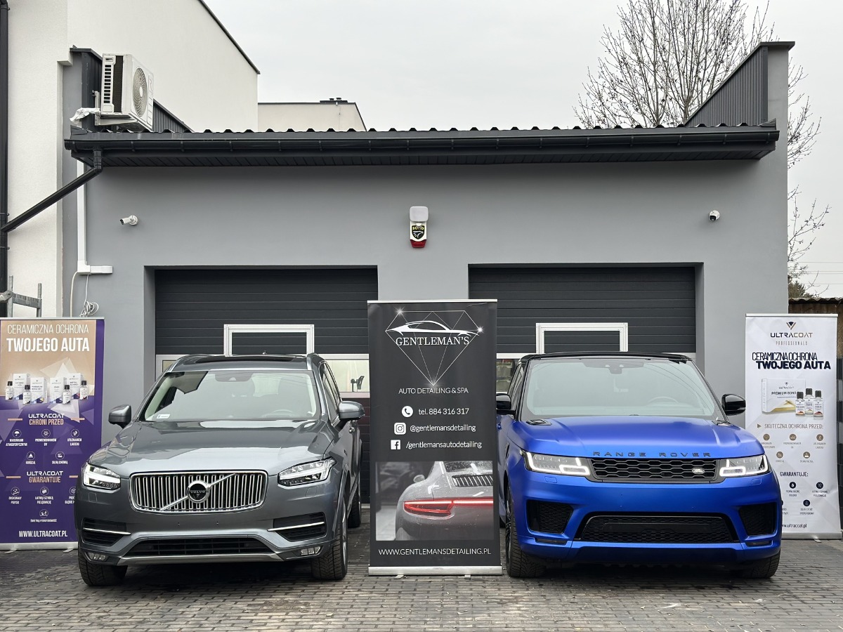 Dwa samochody, szary Volvo XC90 i niebieski Range Rover, prezentowane przed budynkiem z logo Gentleman's Auto Detailing & Spa oraz banerami reklamującymi ceramiczną ochronę Ultracoat.