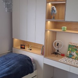 Kuchnie szafy Kita - Białe szafy wnękowe z drewnianymi elementami, zintegrowane z łóżkiem i biurkiem, oświetlenie LED, dekoracje na półkach.