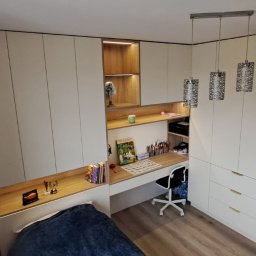 Kuchnie szafy Kita - Pokój młodzieżowy z zabudową meblową: białe szafy z drewnianym biurkiem i półkami, oświetlenie LED w półkach, wiszące lampy dekoracyjne, łóżko z niebieską narzutą, widok z góry.