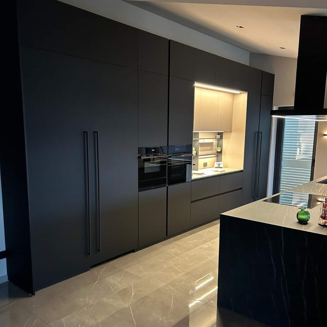 Nowoczesna, minimalistyczna kuchnia w Zabrzu z zabudową w odcieniach grafitu, z długimi, smukłymi uchwytami, wbudowanymi sprzętami AGD i wyspą z marmurowym blatem.