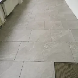 Układanie szarych płytek podłogowych w trakcie prac, widoczne krzyżyki dystansowe i warstwa kleju pod ostatnią płytką.