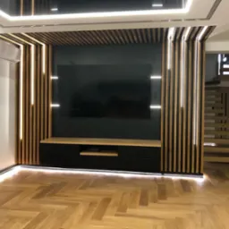 Nowoczesny salon z drewnianą zabudową telewizora z podświetleniem LED, parkietem w jodełkę i schodami w tle.