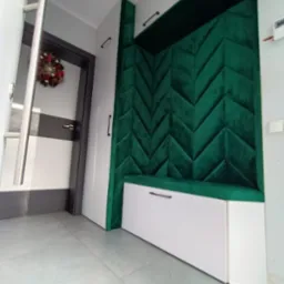 Nowoczesny przedpok&oacute;j z wnęką obitą zielonym, pikowanym materiałem w jodełkę, połączoną z białą szafką z siedziskiem i szafą w zabudowie.