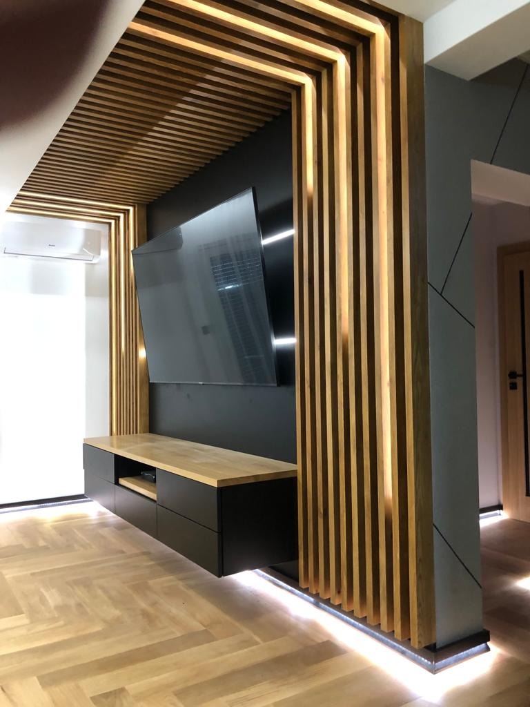 Nowoczesny salon z czarną ścianą telewizyjną, drewnianą zabudową z listew z podświetleniem LED, wiszącą szafką RTV z drewnianym blatem i parkietem ułożonym w jodełkę.