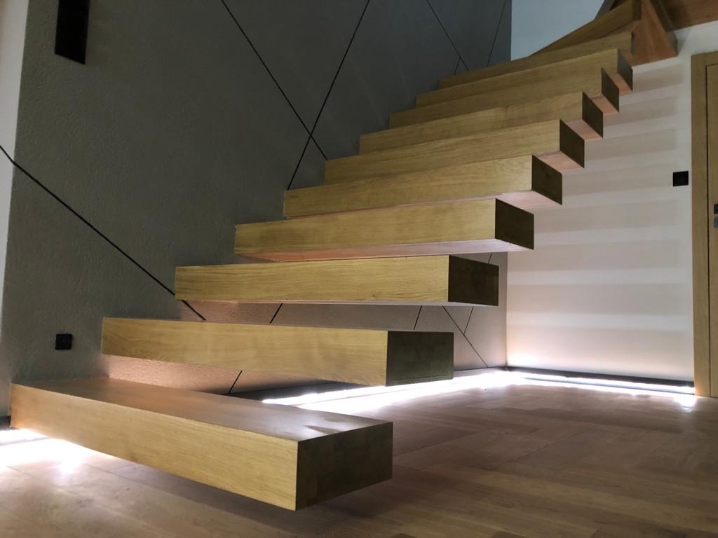 Nowoczesne schody dywanowe z podświetleniem LED, drewniane stopnie o grubym profilu, minimalistyczny design z czarnymi liniami dekoracyjnymi na ścianie.