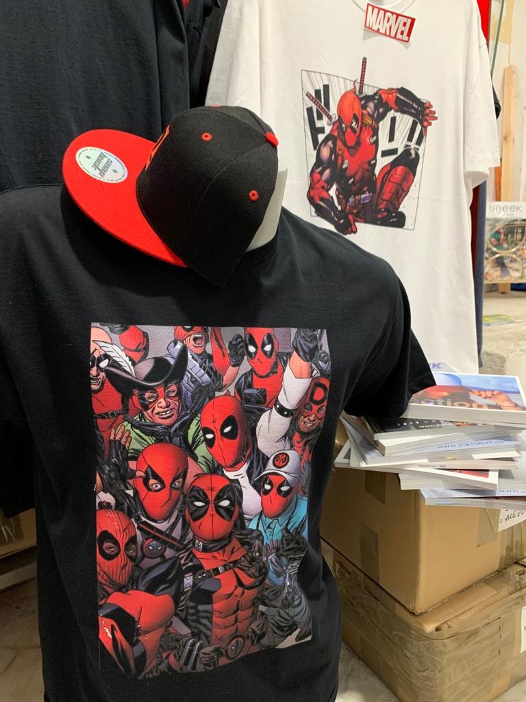 Czarna koszulka z nadrukiem komiksowej postaci Deadpoola w grupie, prezentowana na manekinie z czarno-czerwoną czapką, obok biała koszulka z nadrukiem Deadpoola w stylu mangi.