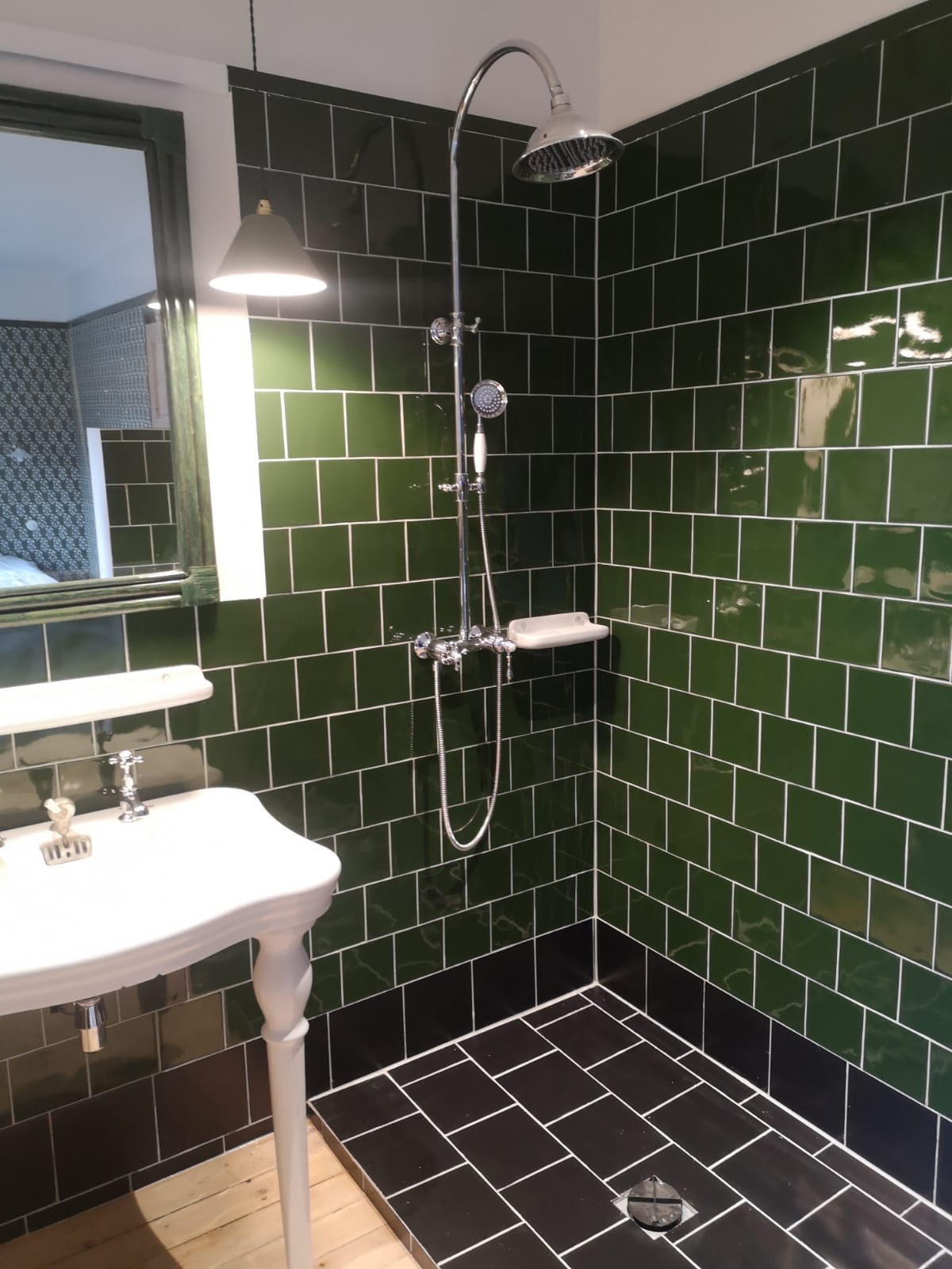 Wykończona łazienka w stylu retro z zielonymi płytkami ściennymi, chromowaną armaturą prysznicową i umywalką na ozdobnych nogach.