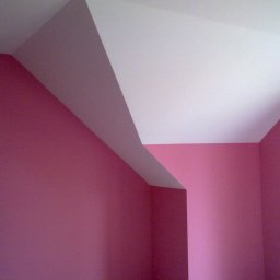 Odnowa - Świeżo pomalowane na różowo ściany w rogu pokoju z białym, skośnym sufitem. Widoczne delikatne niedoskonałości faktury ściany.