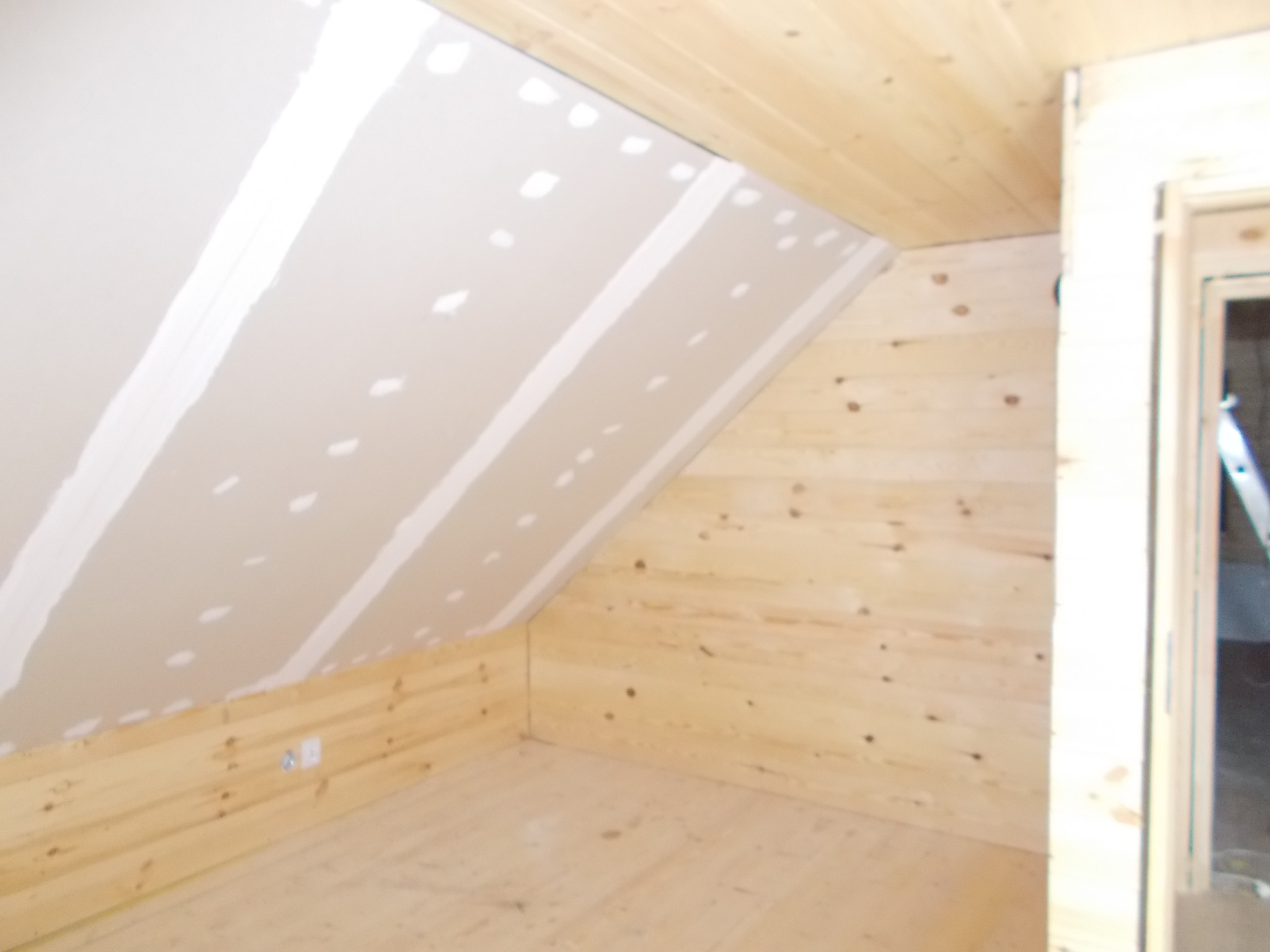 Poddasze z drewnianą boazerią i częściowo zamontowanymi płytami gipsowo-kartonowymi, widoczne łączenia szpachlowane na suficie skośnym.