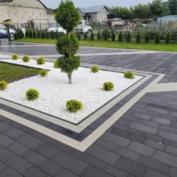 Elegancka posesja z ciemną kostką brukową, białym żwirem i ozdobnymi krzewami. Geometryczny wzór nawierzchni z akcentami jasnych pasów. Estetyczny wygląd.