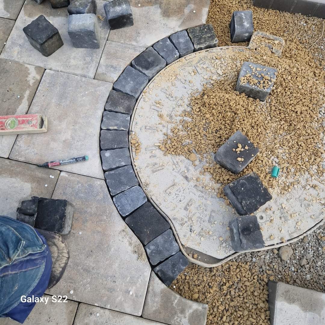 Budowa okrągłego elementu dekoracyjnego z ciemnej kostki granitowej na tle jasnej kostki brukowej, widoczne narzędzia: poziomica i marker.