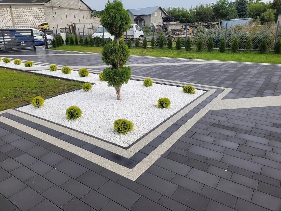 Elegancka posesja z ciemną kostką brukową, białym żwirem i ozdobnymi krzewami. Geometryczny wzór nawierzchni z akcentami jasnych pasów. Estetyczny wygląd.