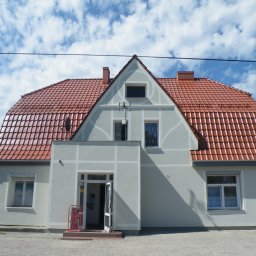 Mat-Bud Sp. z o.o. - Odnowiony budynek z czerwoną dachówką karpiówką i jasnoszarą elewacją w słoneczny dzień z błękitnym niebem i chmurami.