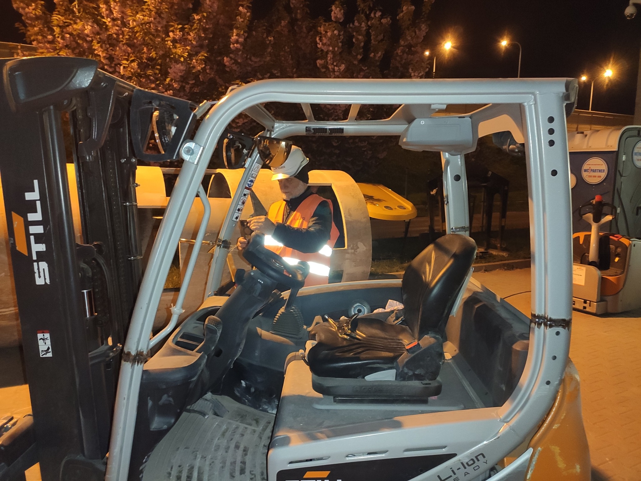 Spawanie kabiny wózka widłowego Still przez spawacza w kamizelce odblaskowej, widoczne ślady spawania na metalowej konstrukcji, oświetlenie nocne.