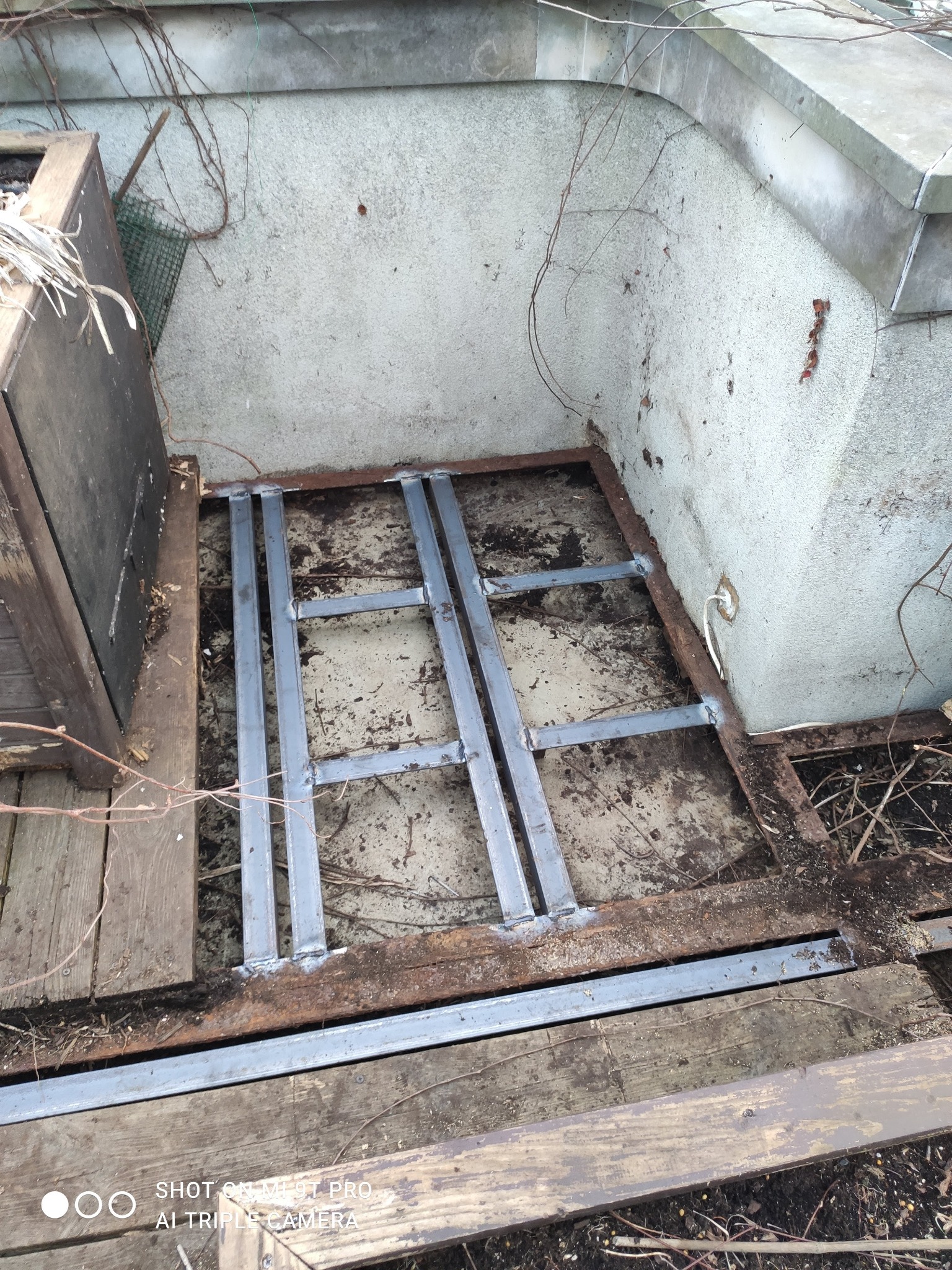 Metalowa konstrukcja spawana na drewnianym podłożu, prawdopodobnie element tarasu lub balkonu. Widoczne ślady spawania i mocowania do starego drewna.