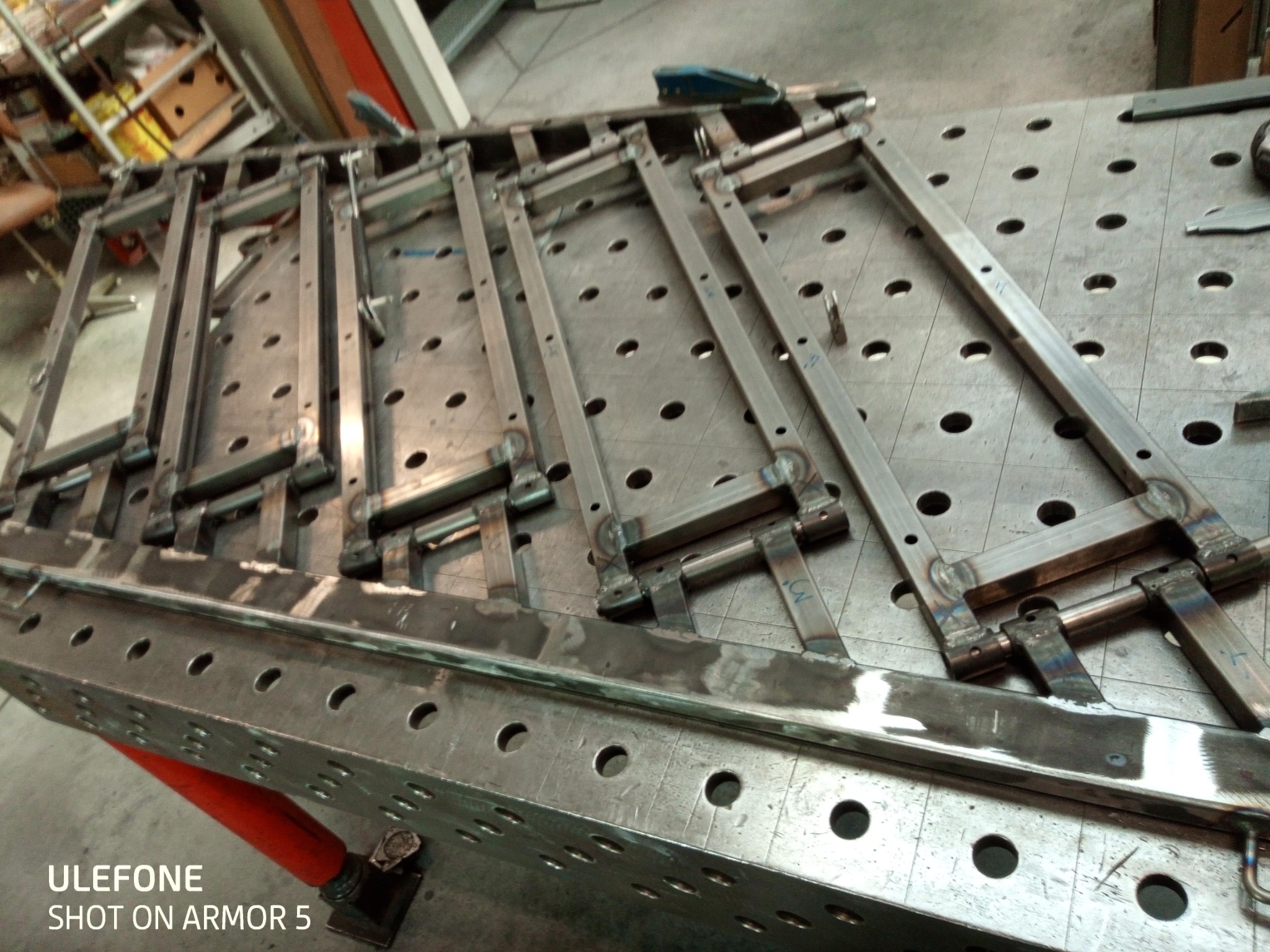 Metalowa konstrukcja spawana z profili na perforowanym stole spawalniczym, widoczne spawy i narzędzia. Elementy przygotowane do dalszej obróbki.