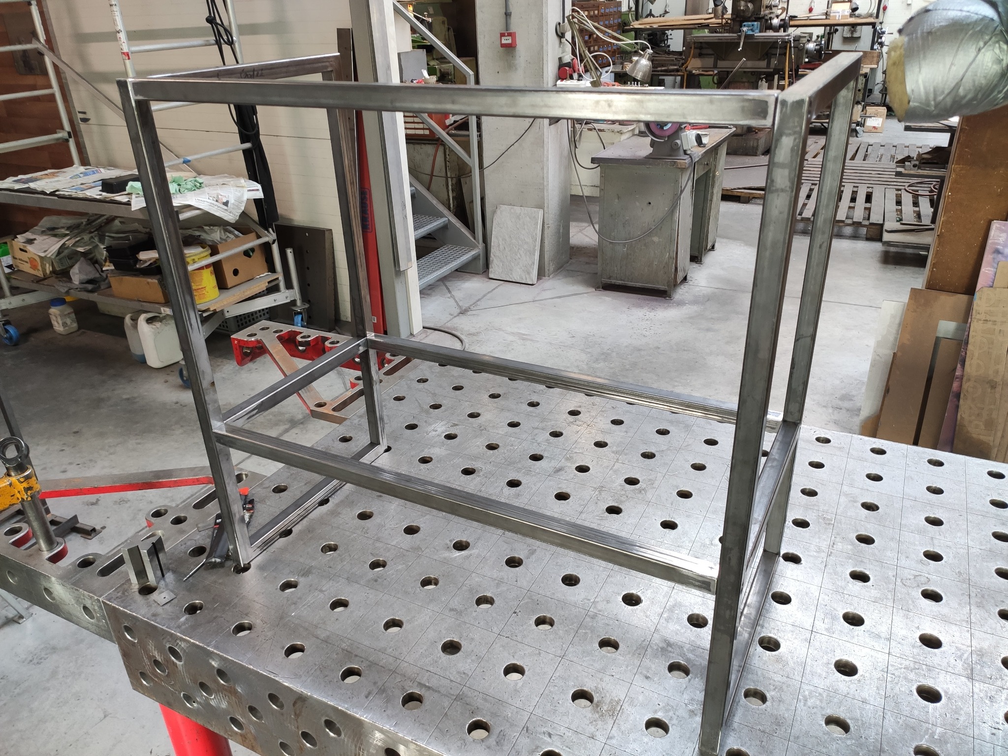 Metalowa konstrukcja spawana z profili na perforowanym stole spawalniczym. Widoczne ślady spawania i narzędzia w tle warsztatu.