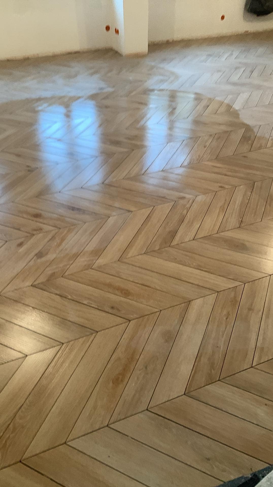 Ułożony parkiet w jodełkę z jasnego drewna, świeżo po lakierowaniu, widoczne odbicia światła, ściany przygotowane do malowania.