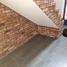 Wykończenie schodów z cegły klinkierowej i płyt gresowych na podłodze, widok z dołu na fragment ściany i podstopnicę.