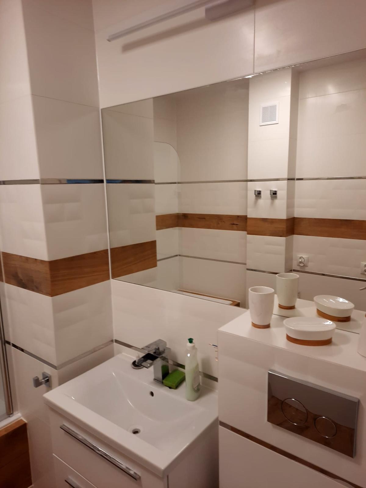 Nowoczesna łazienka w Starym Czarnowie z białymi płytkami z drewnianymi akcentami, lustrem, umywalką z szafką i akcesoriami łazienkowymi.