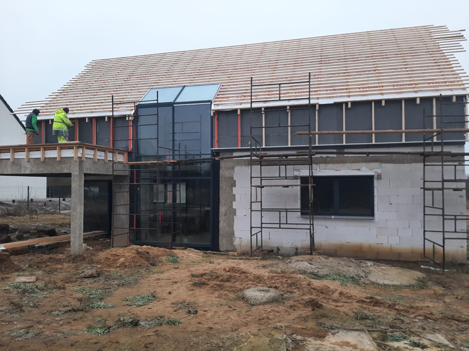 Budowa domu w Starym Czarnowie na etapie montażu więźby dachowej i stolarki okiennej, widoczne rusztowania i pracownicy na balkonie.