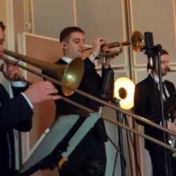 Zespół muzyczny Formacja Rozrywkowa w studiu nagraniowym. Trzech muzyków gra na puzonie, trąbce i saksofonie. W tle mikrofony i panele akustyczne.