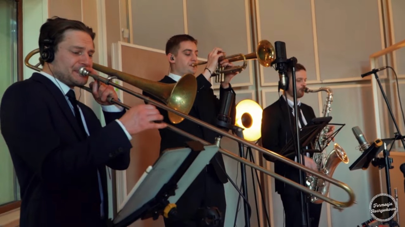 Zespół muzyczny Formacja Rozrywkowa w studiu nagraniowym. Trzech muzyków gra na puzonie, trąbce i saksofonie. W tle mikrofony i panele akustyczne.