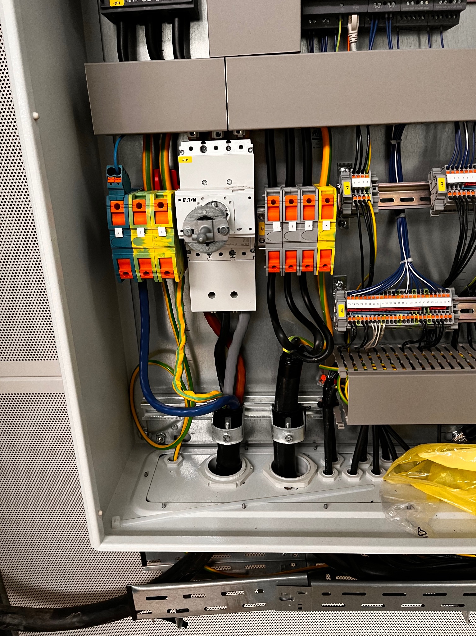 Wnętrze szafy elektrycznej z zainstalowanymi bezpiecznikami, rozłącznikiem Eaton, listwami zaciskowymi i okablowaniem w kolorach niebieskim, żółto-zielonym, czarnym i czerwonym, widoczne również...