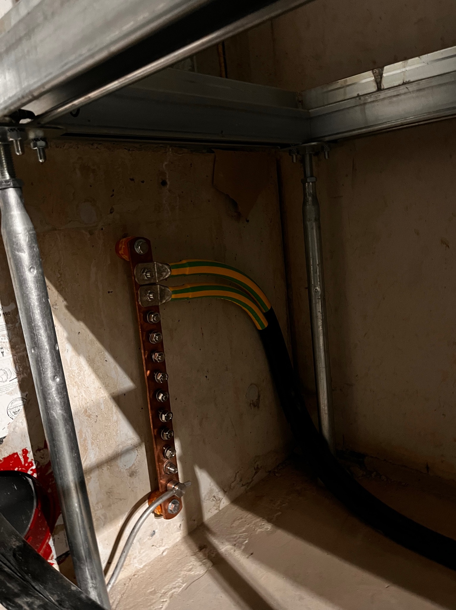 Uziemienie: miedziana szyna z podłączonymi przewodami ochronnymi (żółto-zielonymi) przymocowana do ściany pod konstrukcją sufitu podwieszanego.