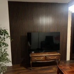 Ściana z dekoracyjnych paneli lamelowych w odcieniach brązu, z widocznym telewizorem i stylizowanymi meblami w salonie.