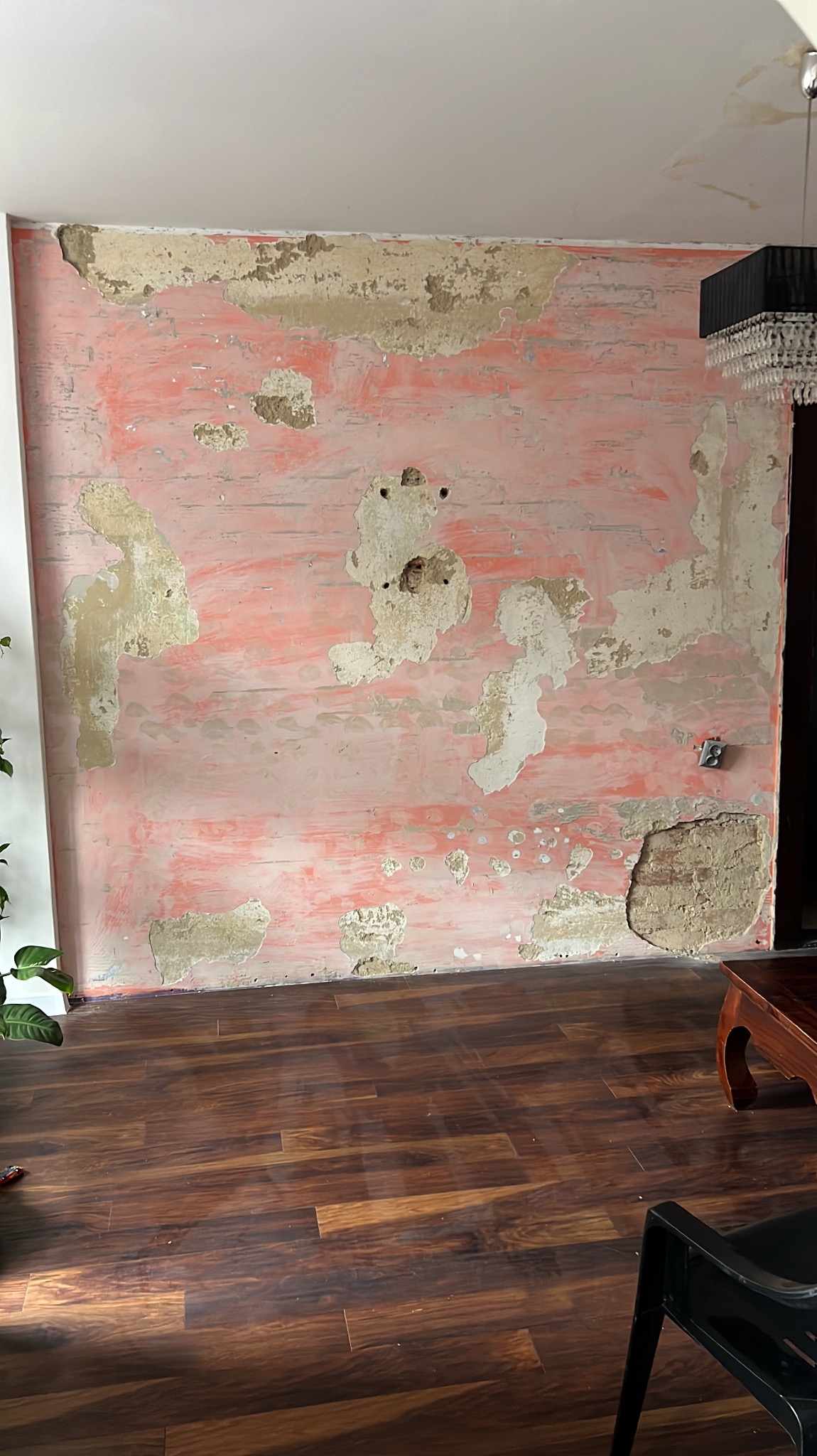 Ściana w trakcie przygotowania do malowania: stara farba odpryskuje, ukazując warstwy poprzednich kolorów i nierówności podłoża, widoczne gniazdko elektryczne.