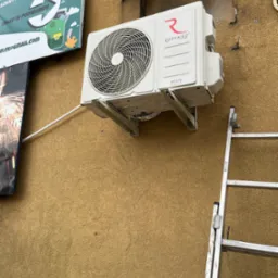 Zamontowana klimatyzacja Rotenso Roni na elewacji budynku, widoczna drabina. Instalacja z rurką odprowadzającą. Nad klimatyzacją szyld reklamowy.