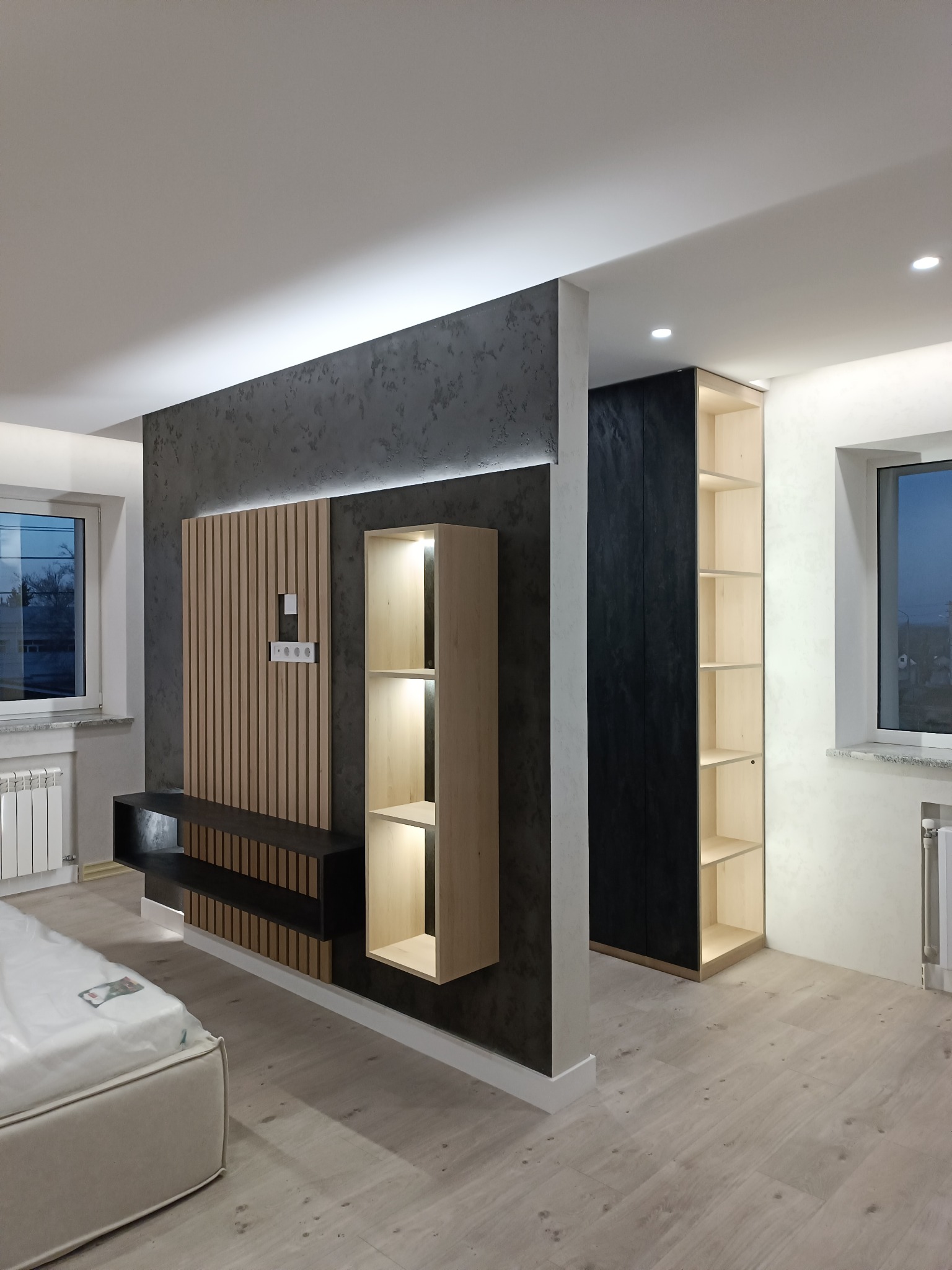 Nowoczesne wnętrze z drewnianą zabudową ściany, półkami z podświetleniem LED i szafą wnękową w minimalistycznym stylu, widok na częściowo umeblowane pomieszczenie.