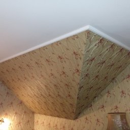 Wojciech Woroniecki - Pokój z beżową tapetą w czerwone kwiaty na ścianach i skośnym suficie, wykończony białym gzymsem.