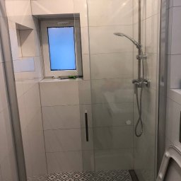 NaVo-Bud - Nowoczesna kabina prysznicowa z deszczownicą i szklanymi drzwiami, jasne płytki ścienne i wzorzysta podłoga, małe okno w kabinie.