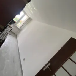 Świeżo pomalowane na biało wnętrze pokoju w Rogoźniku, widoczna drabina malarska przy oknie i częściowo zamontowane ciemne drzwi.