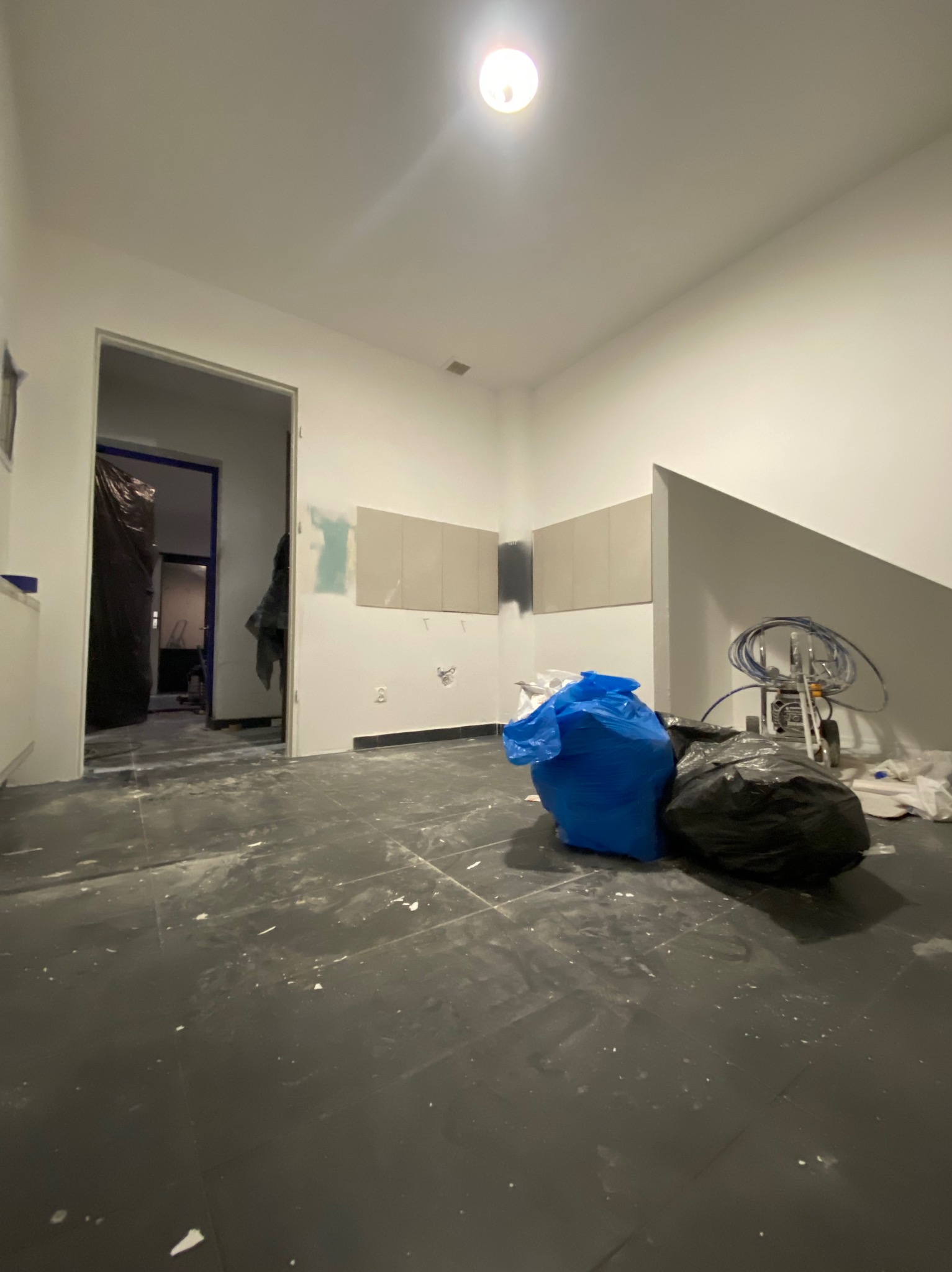 Wnętrze w trakcie prac wykończeniowych: widoczne worki z odpadami, sprzęt malarski, ślady farby na podłodze i fragmentarycznie pomalowane ściany.