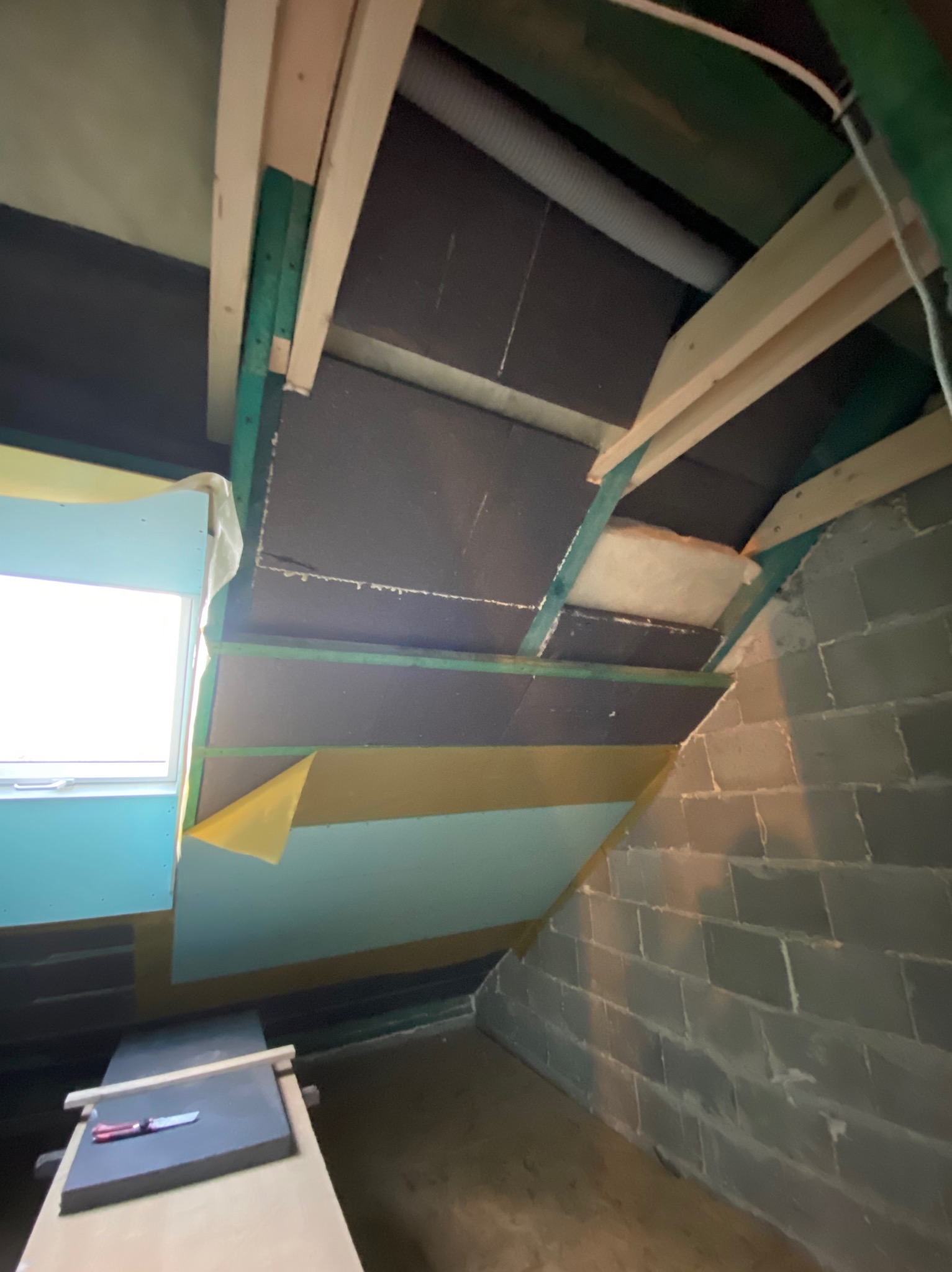 Izolacja poddasza z widocznymi elementami konstrukcyjnymi, folią paroizolacyjną i fragmentem okna dachowego.