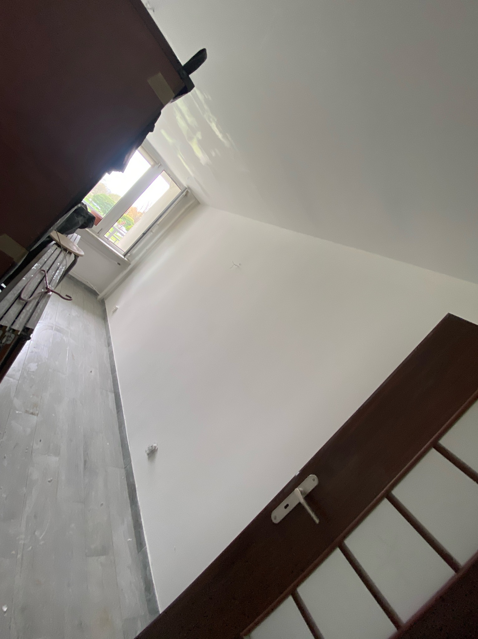 Świeżo pomalowane na biało wnętrze pokoju w Rogoźniku, widoczna drabina malarska przy oknie i częściowo zamontowane ciemne drzwi.