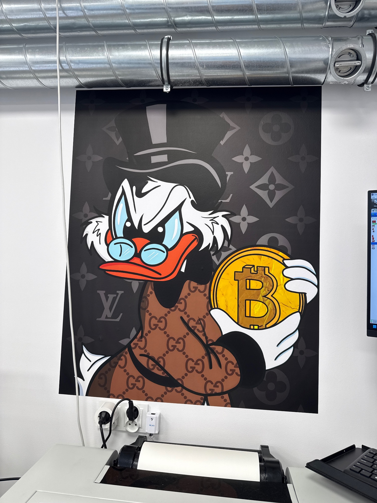 Plakat z kaczką w stylu luksusowych marek, trzymającą monetę Bitcoin, wydrukowany na tkaninie EasyStick. Widoczne przewody i fragment drukarki.