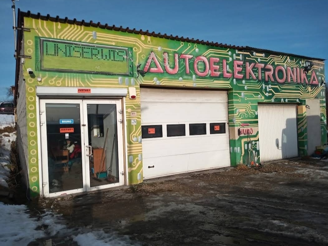 Budynek warsztatu z napisem 'AUTOELEKTRONIKA' oraz grafiką imitującą płytę drukowaną na elewacji, widoczne dwie bramy garażowe i wejście do biura.