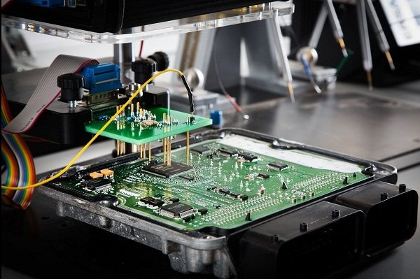Testowanie płytki sterującej silnika samochodowego za pomocą specjalistycznego urządzenia z sondami, widoczne elementy elektroniczne i złącza.