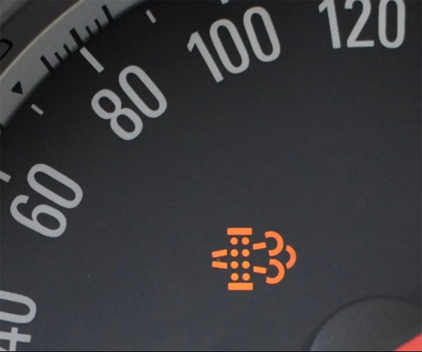 Pomarańczowa kontrolka ostrzegawcza na desce rozdzielczej samochodu, przedstawiająca schematyczny silnik z wydobywającymi się spalinami.