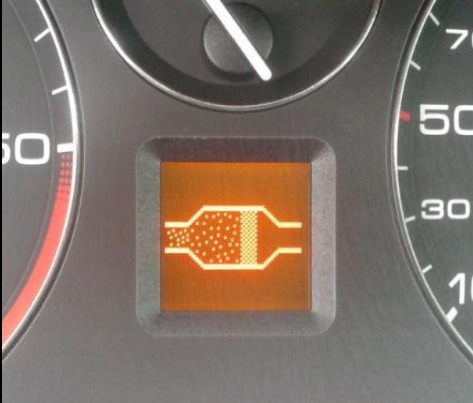 Pomarańczowa kontrolka filtra cząstek stałych (DPF) na desce rozdzielczej samochodu, widoczny fragment prędkościomierza.