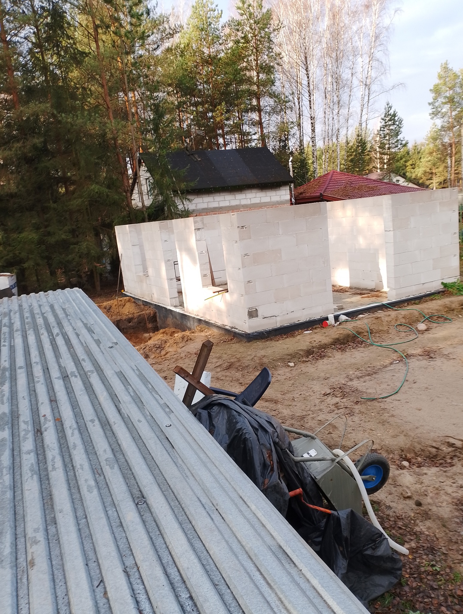 Wznoszenie ścian parteru domu z bloczków silikatowych na fundamencie, widok z góry na plac budowy z elementami składowanymi tymczasowo na pierwszym planie.